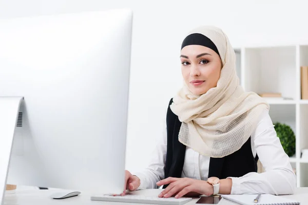 Портрет усміхненої мусульманської бізнес-леді, яка дивиться на камеру під час роботи на комп'ютері в офісі — стокове фото