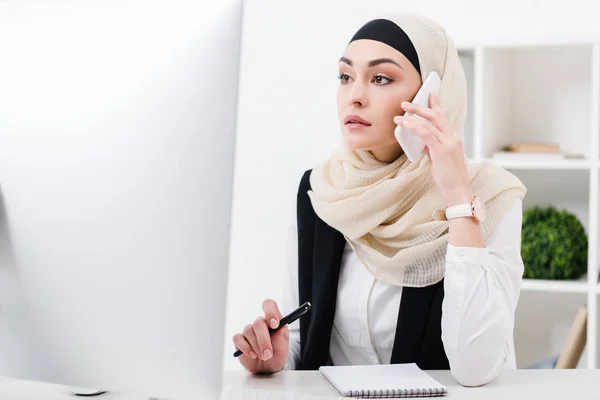 Femme d'affaires concentrée dans hijab parler sur smartphone sur le lieu de travail dans le bureau — Photo de stock