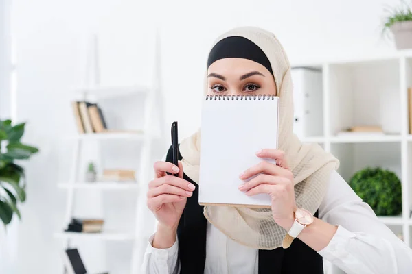 Vista oscurecida de la mujer de negocios árabe con cuaderno vacío en la oficina - foto de stock