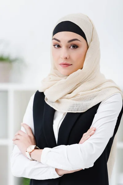 Retrato de mujer de negocios árabe en hiyab con los brazos cruzados de pie en la oficina - foto de stock