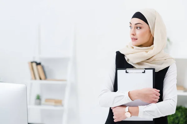 Retrato de mujer de negocios árabe reflexivo con carpeta en las manos en la oficina - foto de stock