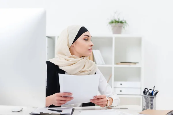 Арабська бізнес-леді з паперами в руках дивиться далеко на робоче місце — стокове фото