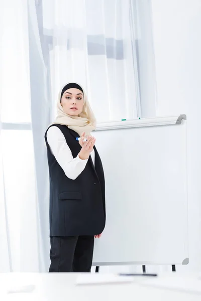Empresária em desgaste formal e hijab de pé na placa branca no escritório — Fotografia de Stock