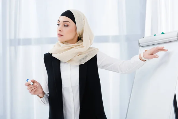 Atraente empresária em hijab apontando para placa branca durante reunião no escritório — Fotografia de Stock