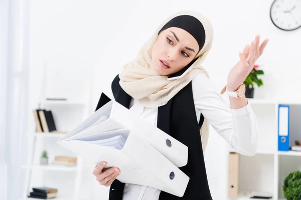 Portrait de femme d'affaires en hijab avec des documents parlant sur smartphone au bureau — Photo de stock