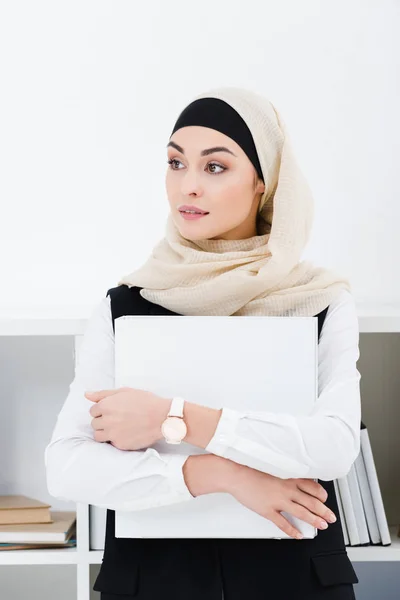 Retrato de pensativa mujer de negocios árabe en hijab con carpeta en las manos en la oficina - foto de stock