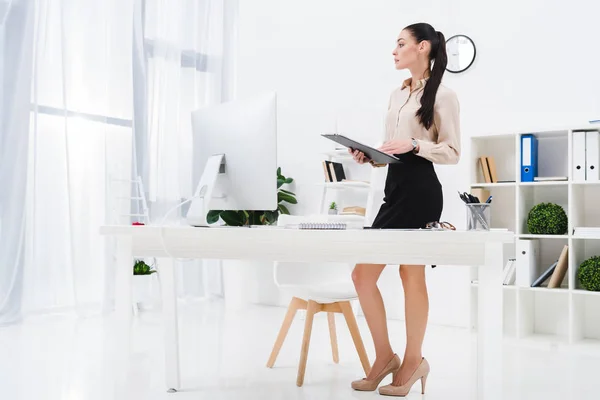 Donna d'affari pensierosa con blocco note in piedi sul posto di lavoro in ufficio — Foto stock