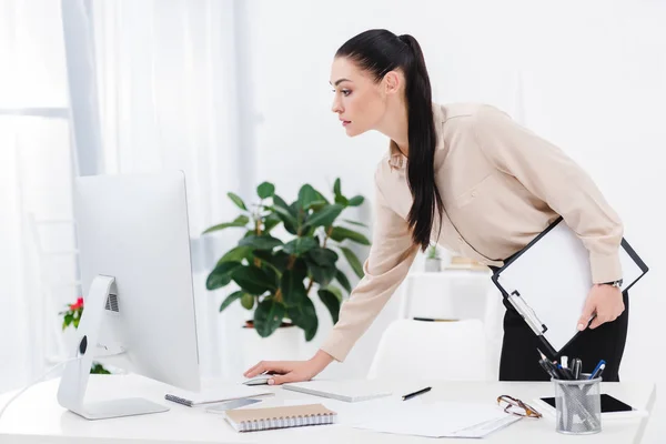 Vista lateral de la mujer de negocios con bloc de notas trabajando en la computadora en el lugar de trabajo - foto de stock