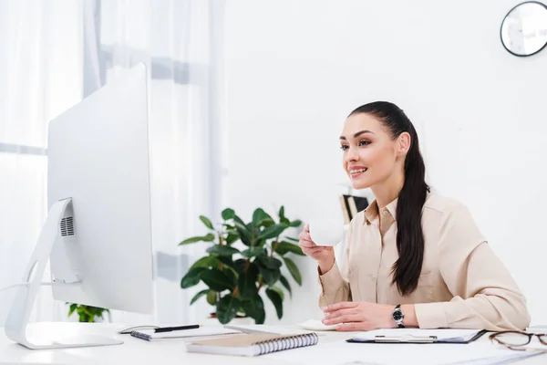 Портрет улыбающейся деловой женщины с чашкой кофе на рабочем месте в офисе — стоковое фото