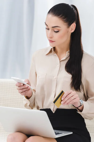 Focused businesswoman with credit card and smartphone making online payment — Stock Photo