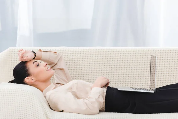 Visão lateral de mulher de negócios com laptop deitado no sofá no escritório — Fotografia de Stock