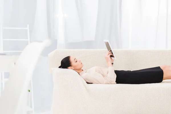 Vue latérale de la femme d'affaires avec tablette numérique couchée sur le canapé dans le bureau — Photo de stock