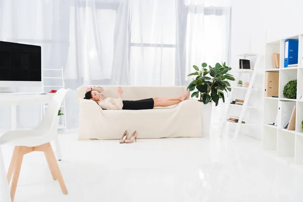 Vue latérale de la femme d'affaires avec tablette numérique couchée sur le canapé dans le bureau — Photo de stock