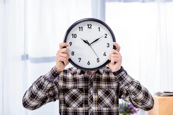 Man holding clock over face in front of window — Stock Photo