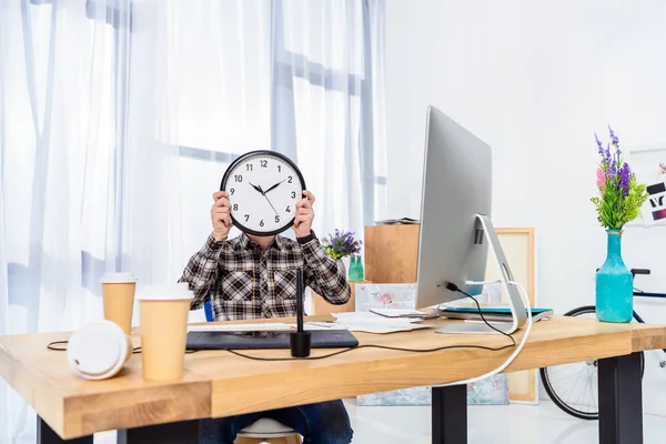 Человек держит часы над лицом в легком домашнем офисе — стоковое фото