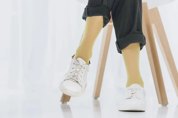 Close-up view of woman sitting on chair with legs in sneakers — Stock Photo