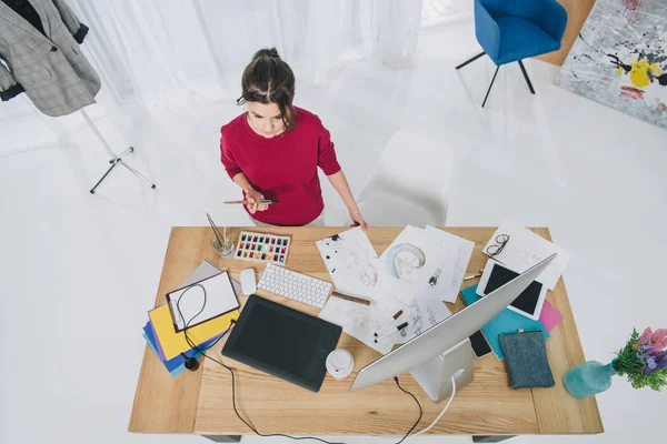 Muchacha joven atractiva que trabaja con bocetos por mesa con ordenador - foto de stock