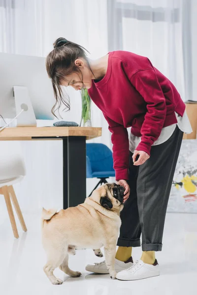 Attractive young girl and cute pug dog by working table — Stock Photo