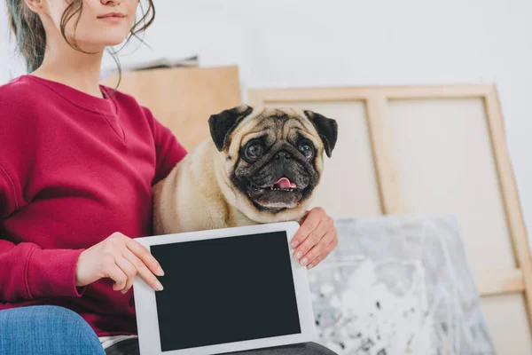 Junge Frau zeigt Tablet-Bildschirm und umarmt Mops Hund — Stockfoto