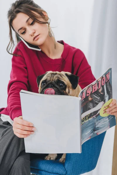Attractive young girl talking on the phone and hugging pug dog — Stock Photo