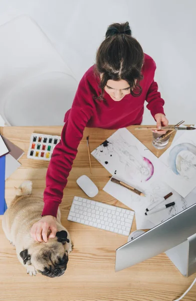 Jeune femme câlin chiot chiot tout en travaillant sur des dessins par table — Photo de stock