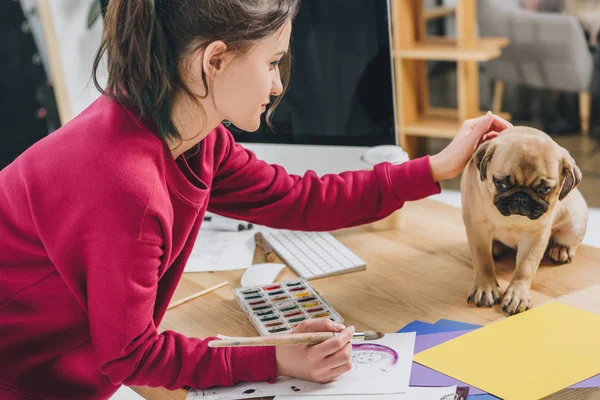 Pretty lady playing with pug while working on illustrations in home office — Stock Photo