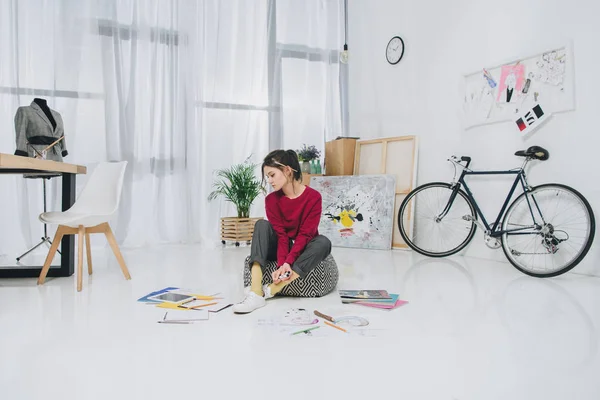 Attractive young girl sitting on floor among sketches — Stock Photo