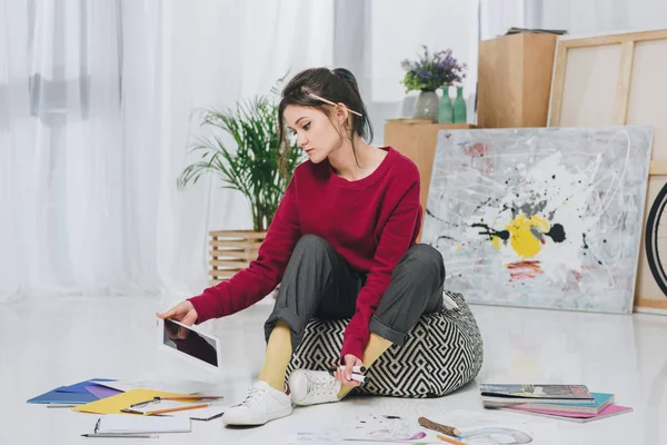 Молодая женщина сидит на полу и держит планшет среди иллюстраций — стоковое фото