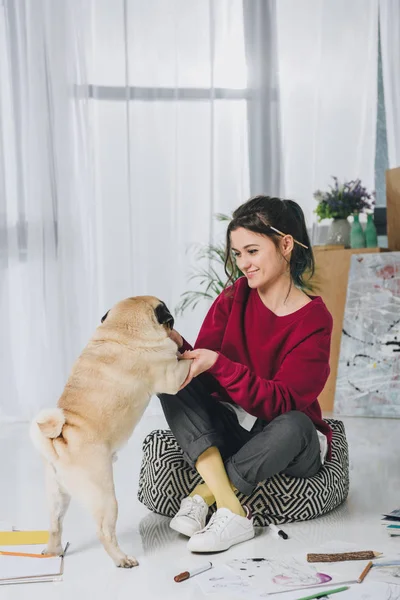 Mujer joven abrazando lindo perro en el suelo entre bocetos - foto de stock