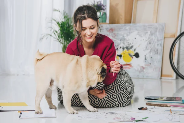 Bella signora che gioca con cucciolo di carlino sul pavimento — Foto stock