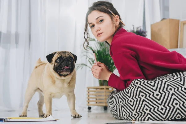 Ilustrador feminino deitado com pug no chão do escritório moderno — Fotografia de Stock