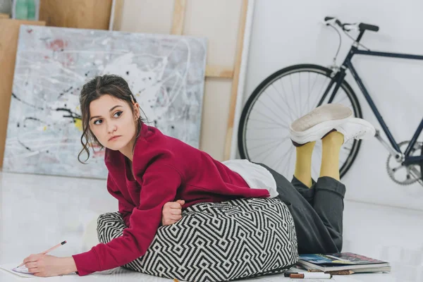 Attractive young girl lying on floor among sketches — Stock Photo