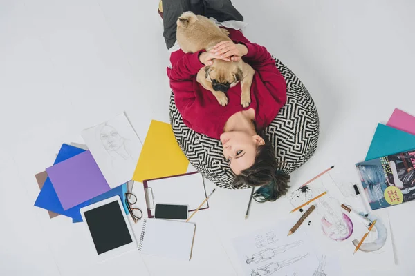 Jeune femme couchée avec carlin parmi les croquis — Photo de stock