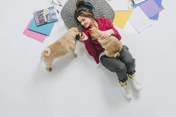 Young woman cuddling pugs on floor among sketches — Stock Photo