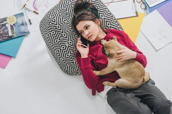 Attractive young girl talking on phone with pug among sketches and magazines — Stock Photo