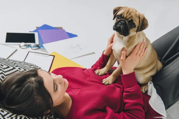 Pretty lady cuddling pug on floor among sketches — Stock Photo