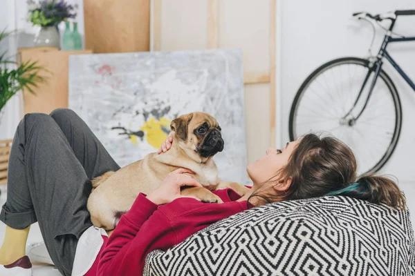 Young woman playing with pug puppy on floor of modern room — Stock Photo