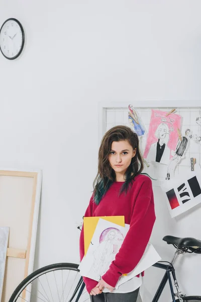Muchacha joven atractiva sosteniendo bocetos en frente del tablero del humor - foto de stock