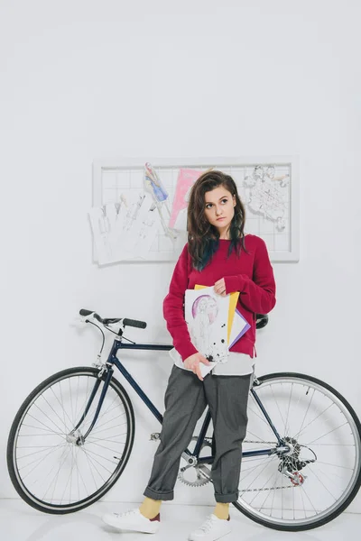 Молодая женщина держит наброски и стоит на велосипеде — стоковое фото