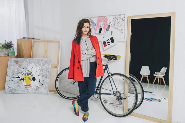 Attractive young girl standing by bicycle in stylish room — Stock Photo