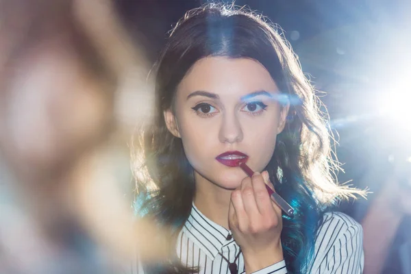 Young girl looking in mirror and applying lipstick — Stock Photo