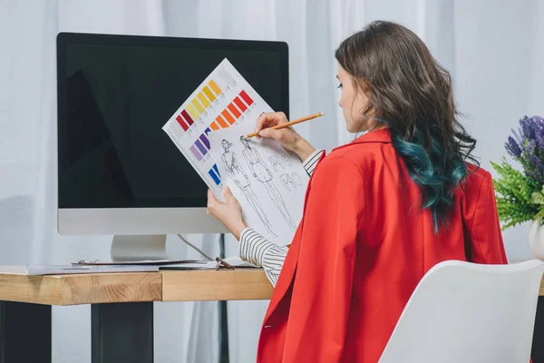 Mujer joven que trabaja con bocetos por mesa de trabajo con ordenador - foto de stock