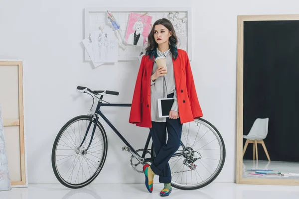 Молодая женщина держит цифровой планшет и чашку кофе на велосипеде — стоковое фото