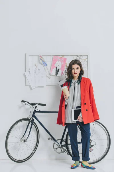 Attrayant jeune fille tenant tablette numérique et tasse de café à vélo — Photo de stock