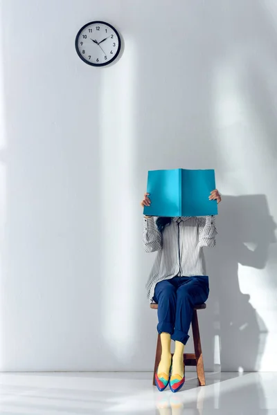 Muchacha joven atractiva leyendo y sosteniendo libro sobre su cara - foto de stock