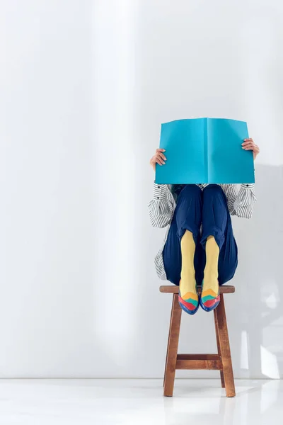 Chica sentada en la silla y leyendo libro - foto de stock