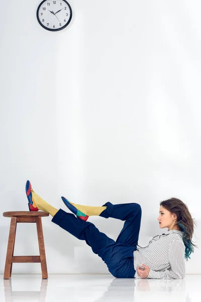 Young woman lying on white floor by wooden chair — Stock Photo