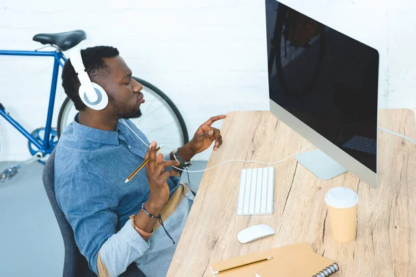 Joven escuchando música en auriculares y trabajando por computadora - foto de stock