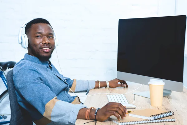 Giovane in cuffia che lavora al tavolo con il computer — Foto stock