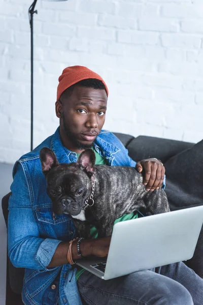 Handsome african american man working on laptop and hugging Frenchie dog — Stock Photo